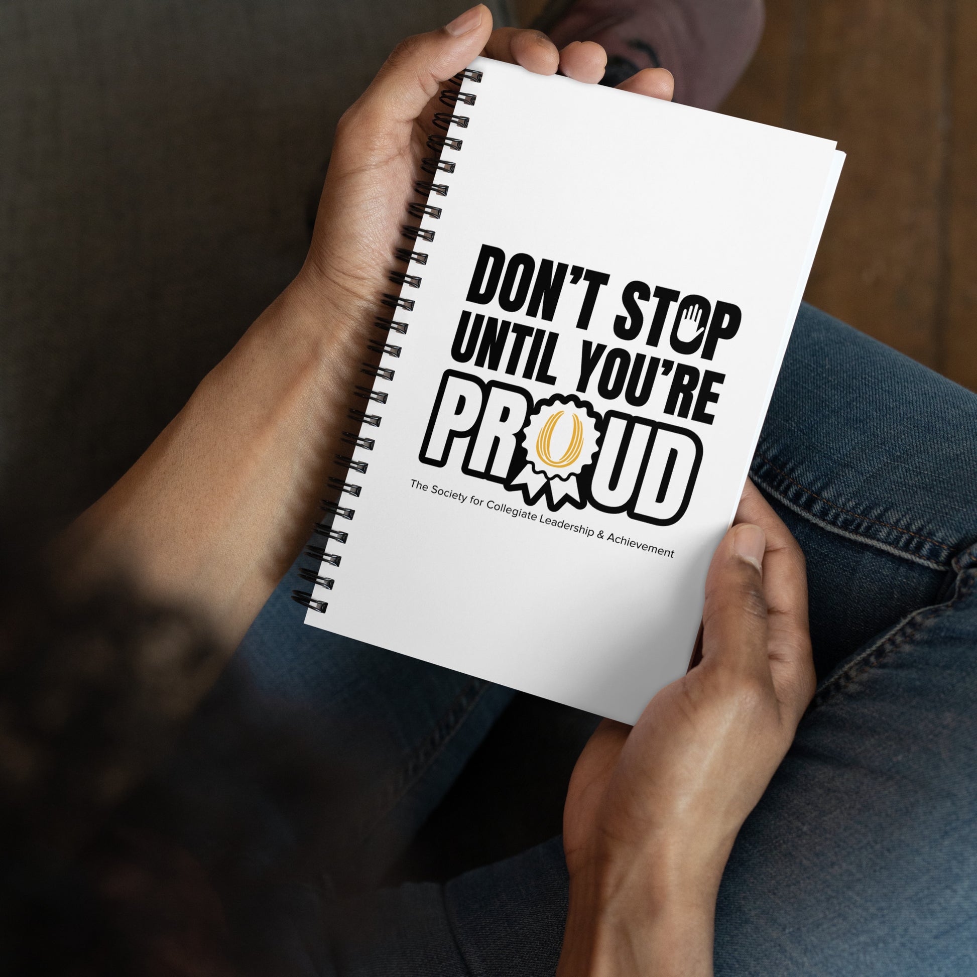 Person holding a notebook with 'Don't Stop Until You're Proud' text