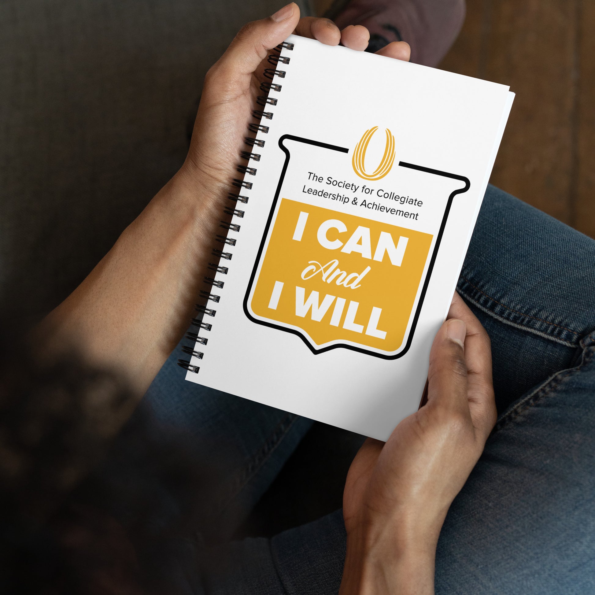 Person holding a notebook with 'I Can And I Will' quote and logo.