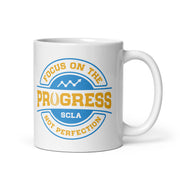 White mug with motivational quote 'Focus on the progress, not perfection' in blue and yellow on a white background